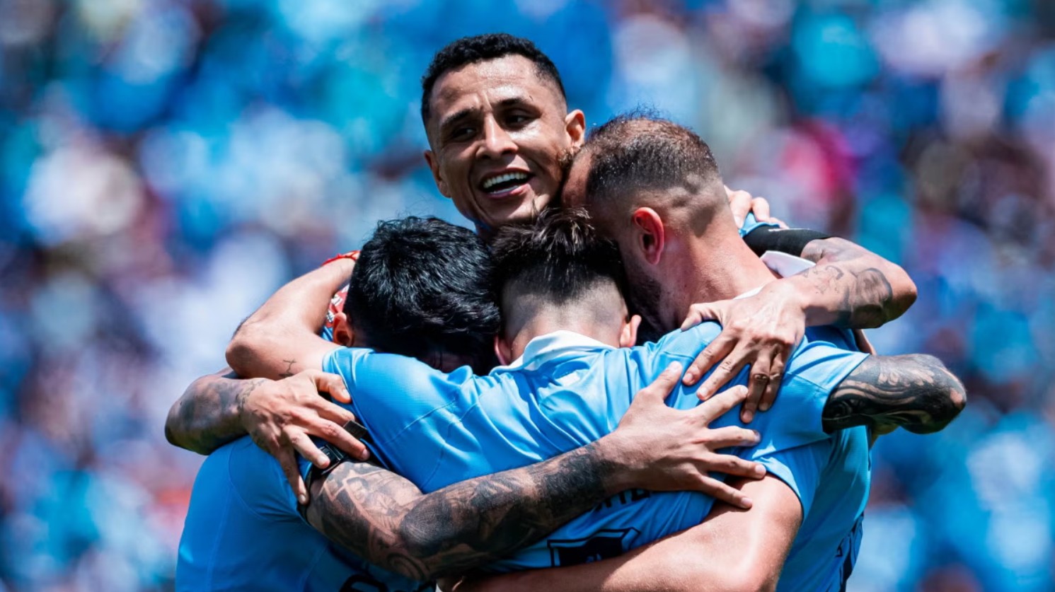 Futbolistas de Sporting Cristal se abrazan durante una celebración en el campo de juego.