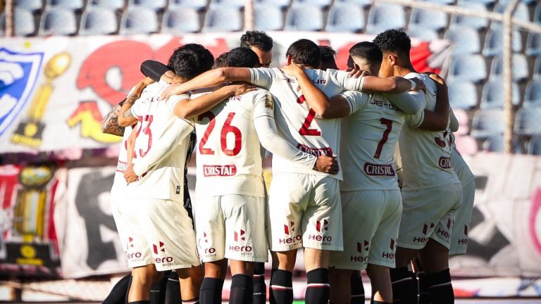 Jugadores de Universitario de Deportes reunidos en círculo y abrazados sobre el campo de juego.